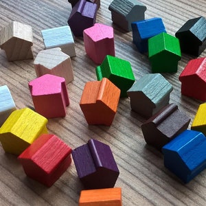 Könnte beinhalten: Eine Sammlung bunter Holzhäuser, jedes in einer anderen Farbe bemalt, darunter Rot, Blau, Grün, Gelb, Orange, Rosa, Lila, Braun, Weiß und Grau. Die Häuser sind in einem zufälligen Muster auf einer Holzoberfläche angeordnet.