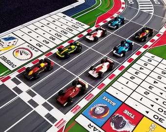 May include: A board game with a race track and colorful toy race cars. The game board has a speedometer, dice, and a track with numbered spaces. The cars are red, yellow, green, blue, and white.