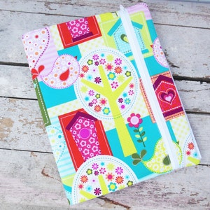 May include: A colorful fabric case with a white zipper. The case features a patchwork design with birdhouses, trees, flowers, and paisley patterns in shades of pink, red, green, yellow, and blue. The case is likely for a tablet or notebook.