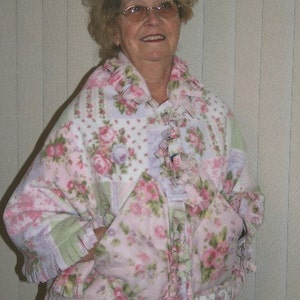 May include: A floral fleece jacket in shades of pink, green, and white. The jacket features a patchwork design with rose patterns, ruffled trim, and pockets. The collar and cuffs are also trimmed with ruffles.