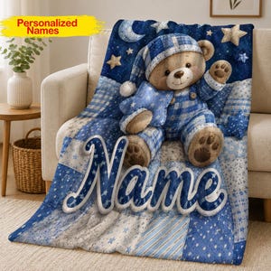 May include: A soft blue blanket featuring a teddy bear wearing a matching plaid nightcap and overalls. The bear holds a blue star. The background is a dark blue night sky with stars and a crescent moon. The word Name is printed in large white letters.