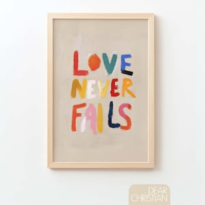 Może przedstawiać: Oprawiony wydruk artystyczny z napisem "LOVE NEVER FAILS" w kolorowej, teksturowanej czcionce. Grafika ma neutralne tło i jasną drewnianą ramę. W prawym dolnym rogu znajduje się napis "DEAR CHRISTIAN".