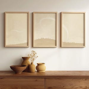 May include: Three framed landscape art prints with a neutral color palette hang above a wooden console. The prints feature a minimalist design with soft, muted tones. Below, a collection of decorative vases and a wooden bowl add to the room's aesthetic.
