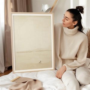 Pode incluir: Uma pintura de aquarela emoldurada de uma paisagem minimalista com uma única figura e um cão à distância. A pintura está em tons de bege e marrom, com um fundo suave e nebuloso.