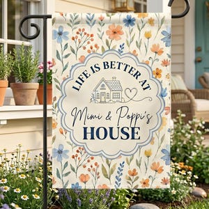 May include: A garden flag with a floral design in shades of blue, orange, and yellow. The flag features the text "LIFE IS BETTER AT Mimi & Poppi's HOUSE" in a decorative font, with a house and heart graphic. The flag is displayed on a black metal stand.