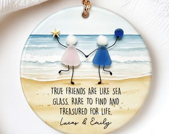 May include: Round ceramic ornament with a beach scene and the text "TRUE FRIENDS ARE LIKE SEA GLASS. RARE TO FIND AND TREASURED FOR LIFE." Two figures hold hands, one with a star, the other with a blue ball. Includes the names "Lucas & Emily".