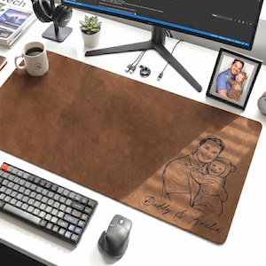 May include: A brown leather desk mat with a keyboard, mouse, and coffee mug on a white desk. The mat features a sketch of a father and child with the text "Daddy & Amelia". A computer monitor, headphones, and a framed photo are also present.