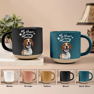 May include: Two ceramic mugs, one black and one teal, each featuring a beagle illustration and the text "My Humans are getting Married!". The mugs have a beige base and a colored handle. Below are mugs in white, orange, yellow, black, and dark blue.