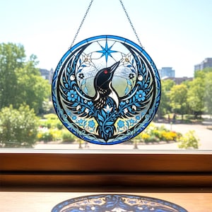 May include: A round stained glass window featuring a black and white bird with a red eye, surrounded by blue floral and leaf designs. The bird is set against a clear background with a blue star at the top. A chain is attached for hanging.