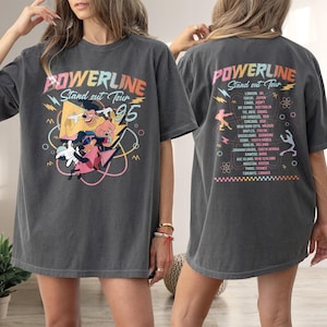 May include: A grey t-shirt with a graphic print of cartoon characters and the text "POWERLINE Stand out Tour 95". The back of the shirt has a list of cities and countries on the "POWERLINE Stand out Tour".