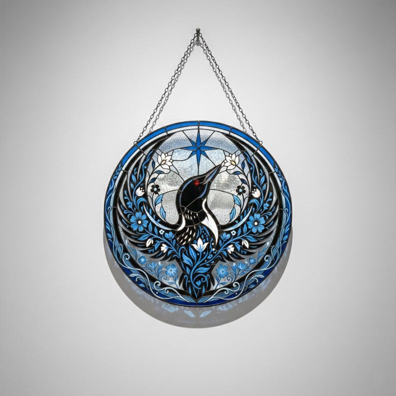 May include: Round stained glass art piece featuring a black bird with red eyes and white accents, surrounded by blue floral and leaf designs. The bird is set against a clear background with a blue starburst design. A silver chain is used for hanging.