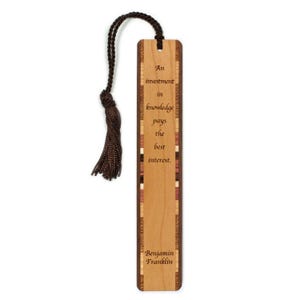 May include: Wooden bookmark with a dark brown tassel. The bookmark has a light wood grain with a decorative border and the quote "An investment in knowledge pays the best interest." by Benjamin Franklin.