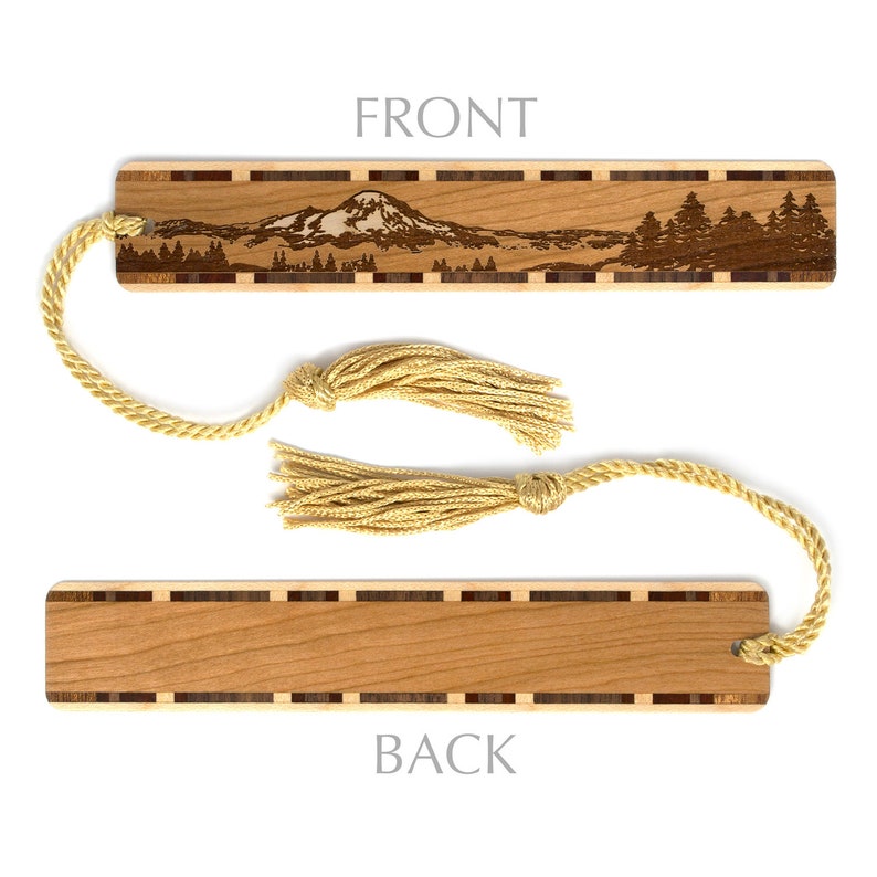 May include: Wooden bookmark with a laser-engraved image of a mountain range and trees. The bookmark has a brown wood grain and a gold tassel. The back of the bookmark is plain wood.