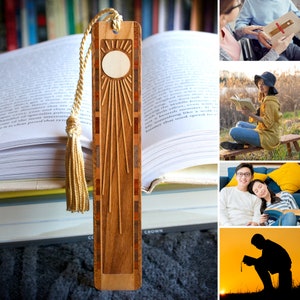 K&ouml;nnte beinhalten: Ein Holz-Lesezeichen mit einem Sonnenmotiv und einem Quasten. Das Lesezeichen besteht aus verschiedenen Holzarten, die ein einzigartiges Muster bilden. Das Lesezeichen ist auf einem Stapel B&uuml;cher abgebildet.
