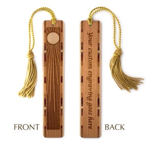 K&ouml;nnte beinhalten: Ein Holz-Lesezeichen mit einem Sonnenmotiv auf der Vorderseite und dem Text "Your custom engraving goes here" auf der R&uuml;ckseite. Das Lesezeichen hat einen goldenen Quasten.