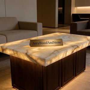 May include: A rectangular coffee table with a glowing, off-white stone top and dark brown wooden base. The table has a built-in light source, and a gold sign that reads "AuraWoodAndStone" is on the top.