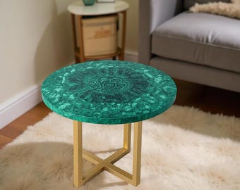 May include: A round side table with a green malachite top and gold-colored metal legs. The table has a decorative pattern on the tabletop and is set on a fluffy, white rug. The table is approximately 20 inches in diameter.