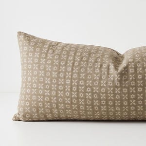 May include: A rectangular throw pillow in a muted taupe color featuring a repeating pattern of small, light-colored floral and geometric shapes arranged in vertical columns across the entire surface of the fabric cover.