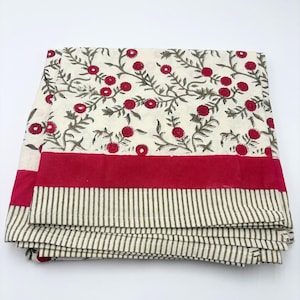 Può includere: Tessuto bianco piegato con un motivo floreale di fiori rossi e foglie verdi. Un ampio bordo rosso e un bordo a righe in verde e bianco completano il design. Il tessuto è piegato ordinatamente.
