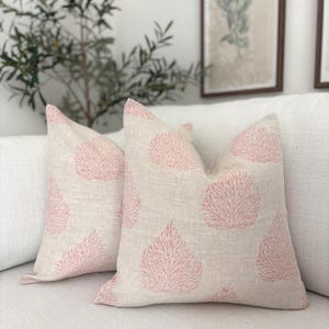 May include: Two decorative throw pillows with a light beige linen fabric and a pink coral reef pattern.