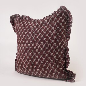 May include: A burgundy pillow with a white floral pattern and a ruffled edge.