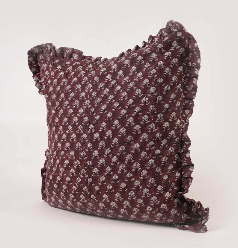 May include: A burgundy pillow with a white floral pattern and a ruffled edge.
