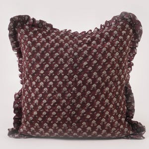 May include: A burgundy pillow with a white floral pattern and a ruffled edge.