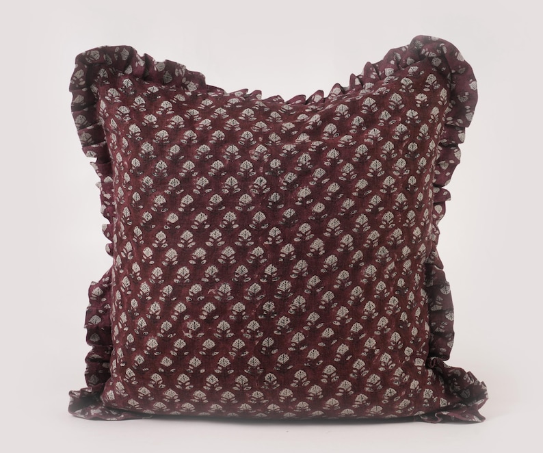 May include: A burgundy pillow with a white floral pattern and a ruffled edge.