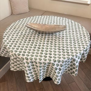 May include: A white round tablecloth with a green floral pattern. A silver serving bowl is on top of the tablecloth.