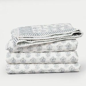 May include: A stack of four white and gray patterned quilts. The top quilt features a striped border and floral design. The other three quilts have a repeating floral pattern. The quilts are folded neatly, showcasing the intricate designs.