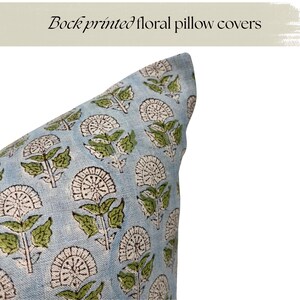 May include: Close-up of a light blue pillow cover with a repeating floral pattern. The design features white and brown flower shapes with green leaves. The text "Block printed floral pillow covers" is at the top.