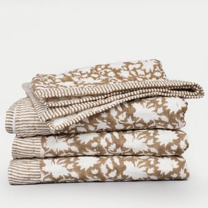 May include: A stack of four folded quilts. The quilts feature a white background with a brown floral pattern. One quilt has brown and white stripes. The quilts are stacked on top of each other.
