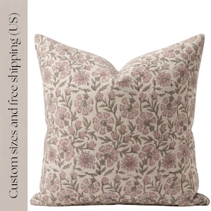May include: Square decorative pillow with a floral pattern in shades of pink and gray on a cream background. The pillow features a repeating design of stylized flowers and leaves, creating a soft, inviting aesthetic. The pillow is a square shape.