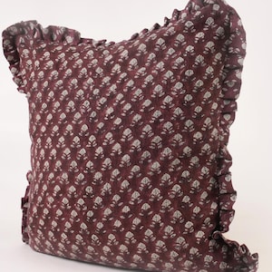 May include: A burgundy pillow with a white floral pattern and a ruffled edge.