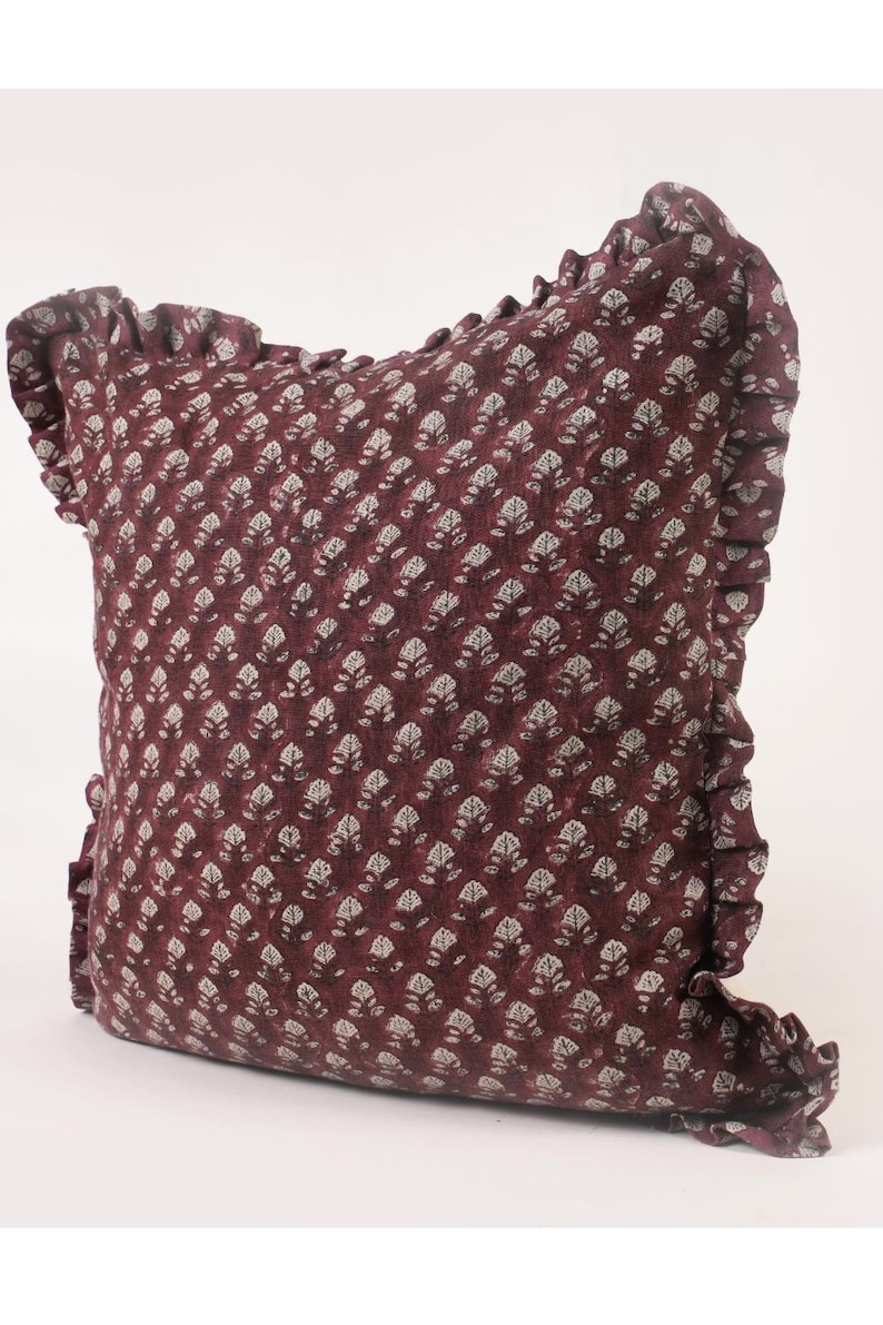 May include: A burgundy pillow with a white floral pattern and a ruffled edge.