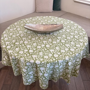 May include: A round green tablecloth with a white floral pattern. The tablecloth is laid on a table with a silver bowl in the center.