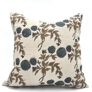 Op de afbeelding: Een beige linnen kussenhoes met een bloemenpatroon. De bloemen zijn donkerblauw en de stelen zijn bruin.