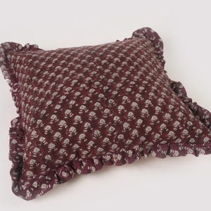 May include: A burgundy pillow with a white floral pattern and a ruffled edge.