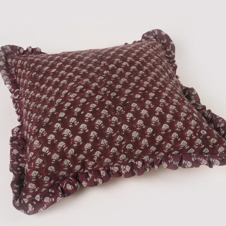 May include: A burgundy pillow with a white floral pattern and a ruffled edge.