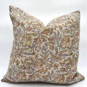 May include: A decorative throw pillow with a floral pattern in shades of brown, yellow, and gray on a beige background.