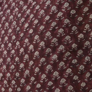 May include: A close-up of a burgundy fabric with a white floral pattern. The fabric has a subtle texture and a repeating pattern of small, stylized flowers.
