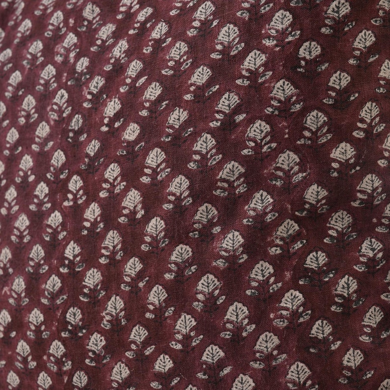 May include: A close-up of a burgundy fabric with a white floral pattern. The fabric has a subtle texture and a repeating pattern of small, stylized flowers.