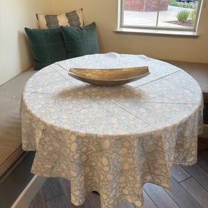 May include: A round table with a blue and white floral tablecloth. A silver serving bowl sits in the center of the table.