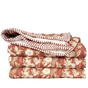 May include: A folded quilt featuring a terracotta red background with a repeating white and light green floral pattern. The edges are finished with a white and terracotta red striped border, and the reverse side is a solid white fabric.