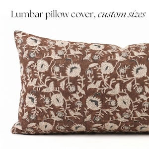 Pode incluir: Uma capa de almofada lombar retangular com fundo castanho e um padrão floral repetitivo em creme. O texto "Lumbar pillow cover, custom sizes" está impresso a preto acima da capa da almofada sobre um fundo branco liso.