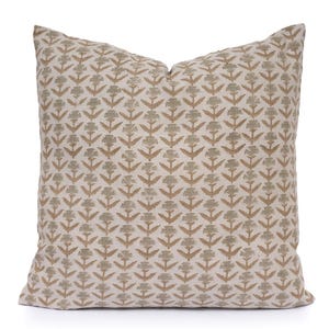 May include: Square decorative pillow with a repeating floral pattern in shades of beige, tan, and muted green. The pillow has a soft, textured appearance and is likely made of fabric. The floral design is symmetrical and covers the entire surface.