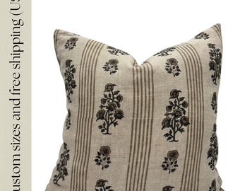 May include: A square cushion with a beige background and vertical brown stripes. The cushion features a repeating pattern of dark brown floral designs. The cushion is a neutral colour and would complement any decor.