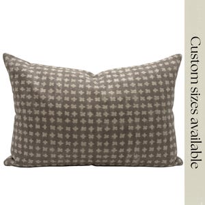Könnte beinhalten: Ein rechteckiges Zierkissen mit taupefarbenem Hintergrund und einem sich wiederholenden Muster aus kleinen, cremefarbenen Blumenformen. Das Kissen hat ein weiches, strukturiertes Aussehen. Der Text "Custom sizes available" ist vertikal auf der rechten Seite gedruckt.