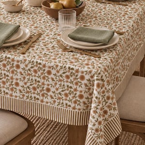 May include: A rectangular tablecloth featuring a white base with a repeating pattern of small brown flowers and green leaves. The edges are finished with a wide border of vertical brown and white stripes. The fabric drapes over a wooden table.