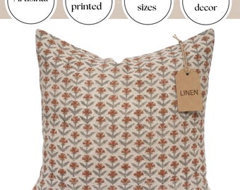 May include: Square linen cushion featuring a repeating floral design in rust, grey, and cream. The cushion has a tag that reads "LINEN". The cushion is hand printed and suitable for farmhouse decor.